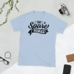 Flat lay of light blue "The Spare Human" minimalist t-shirt with scissors and plant on white background