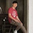 Young man sitting on stairs wearing heather red "My Cat’s Plus One" shirt in urban setting