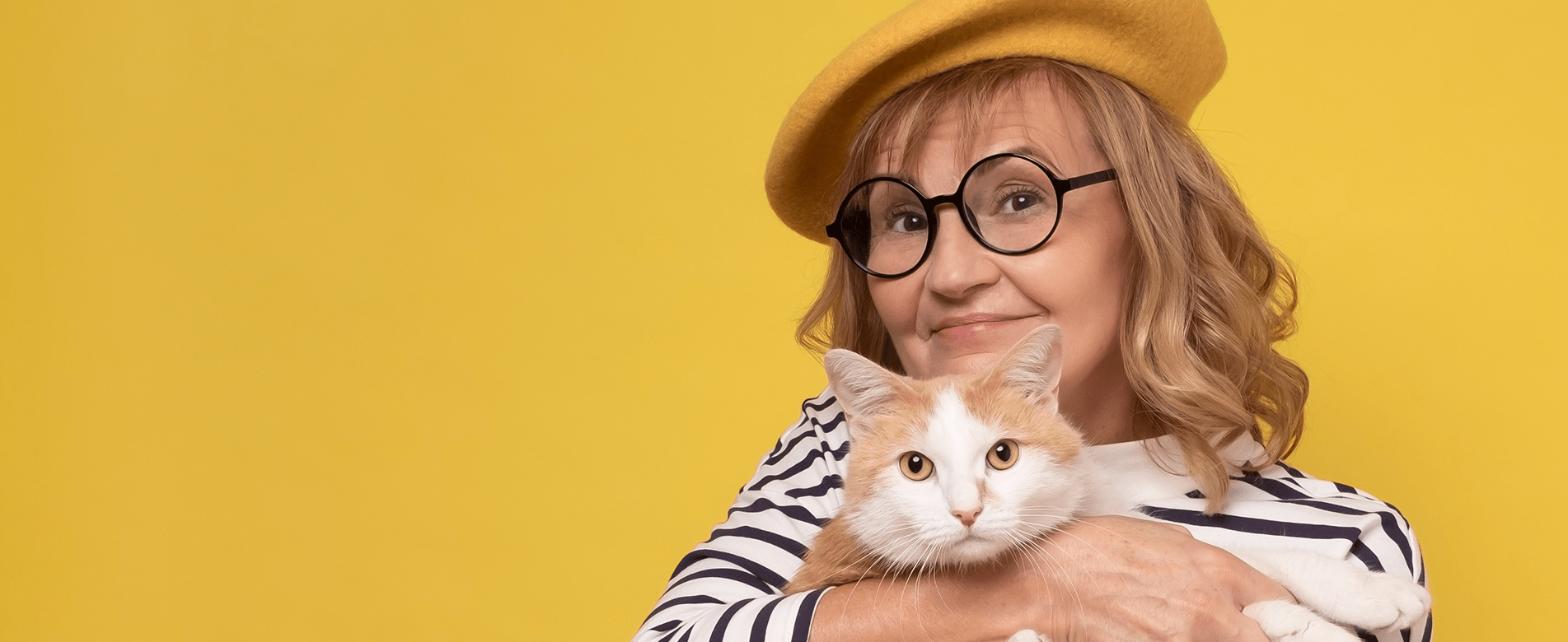 Smiling woman in glasses and yellow beret hugging orange and white cat – Spare Human Society pet parent club.