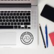 Spare Human Society sticker placed on silver laptop next to keyboard and pens