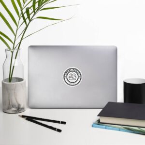 Spare Human Society vinyl sticker centered on silver laptop near books and plant