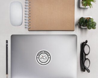 pet-parent-logo-sticker-on-laptop-modern-workspace Black and white Spare Human Society logo decal on laptop with glasses and notebook