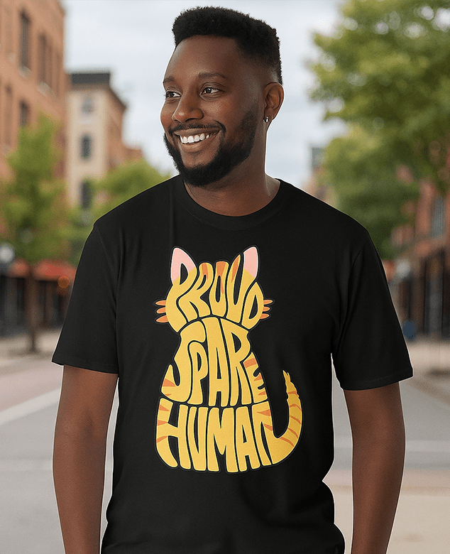Smiling man wearing a black “Proud Spare” t-shirt with yellow lettering from Spare Human Society, standing outside on a sunny day.