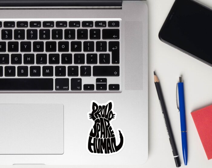 funny-cat-laptop-decal-proud-spare-human. Proud Spare Human cat sticker displayed next to trackpad on a silver laptop