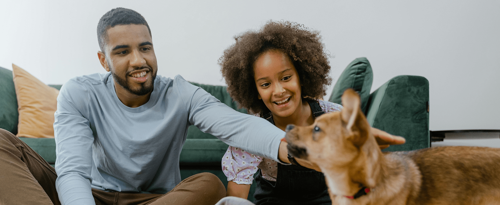 Smiling man and child playing with a happy rescue dog on a green couch, representing how every purchase helps give pets a second chance at life.